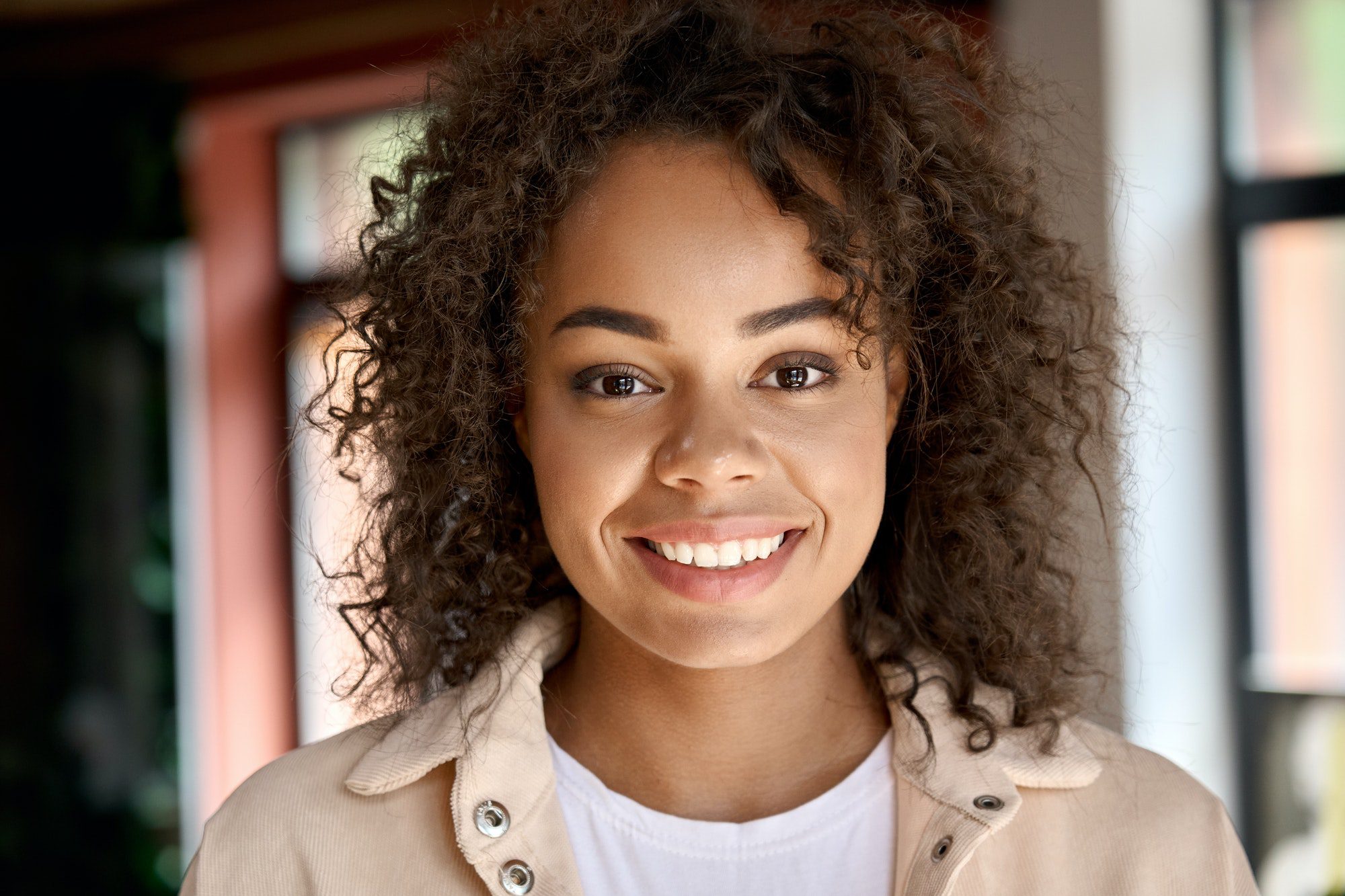 Headshot portrait of young African American woman looking at camera indoors.