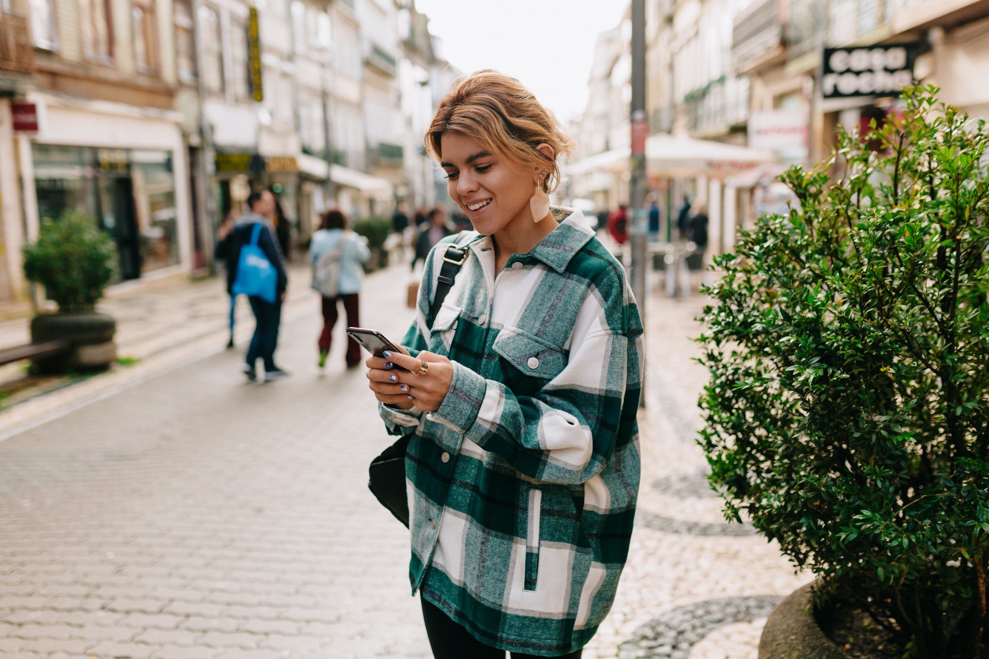 Stylish pretty european woman walking past european streets with smartphone.